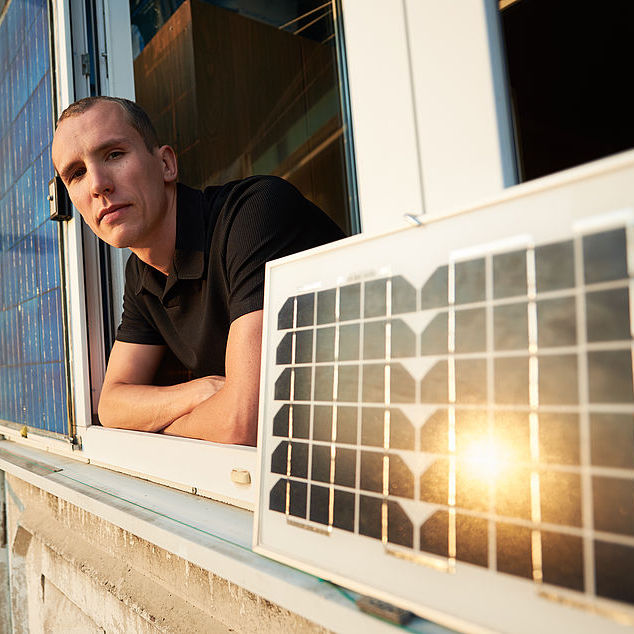 Man on balcony of residential building with solar panel in which the sun is reflected at sunset. Guy looking to the camera. Concept converting solar radiation into electricity